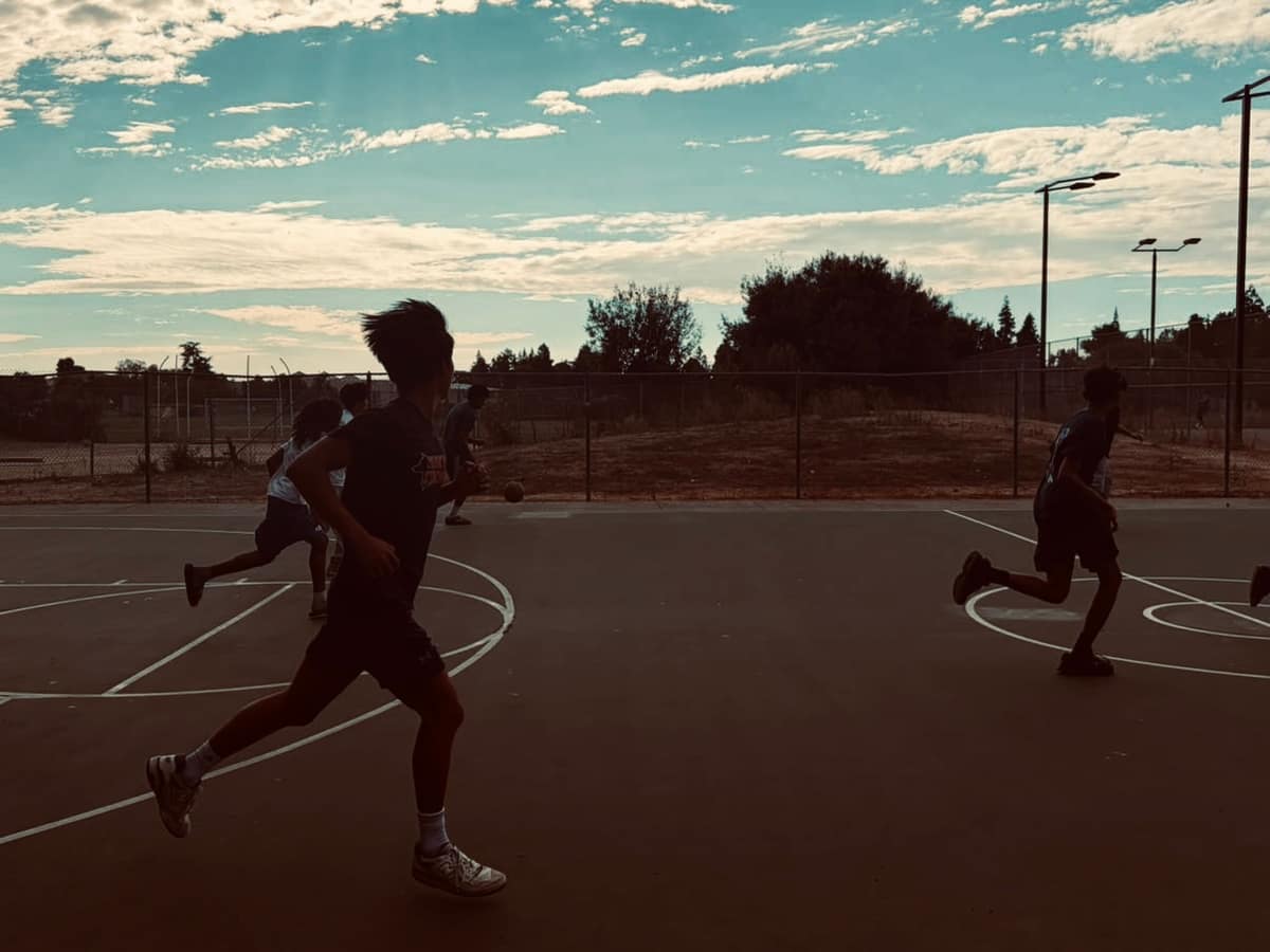 Players running the length of an outdoor basketball court at dusk