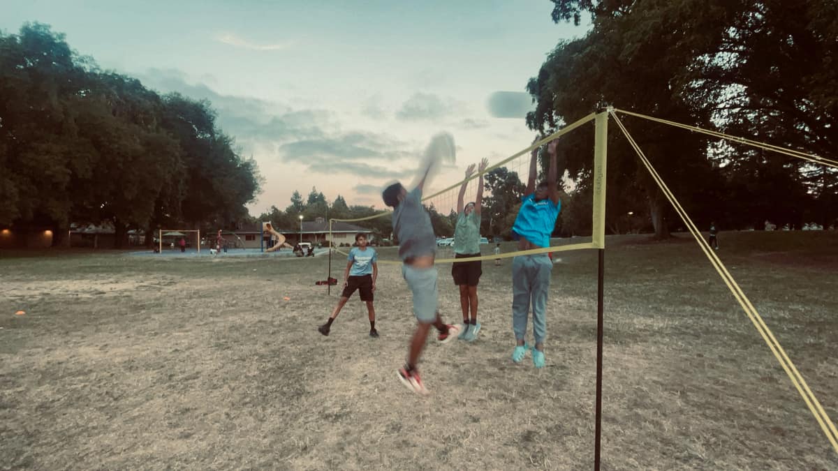 A player mid-jump spiking at the net during an evening volleyball game on grass at a Fremont park
